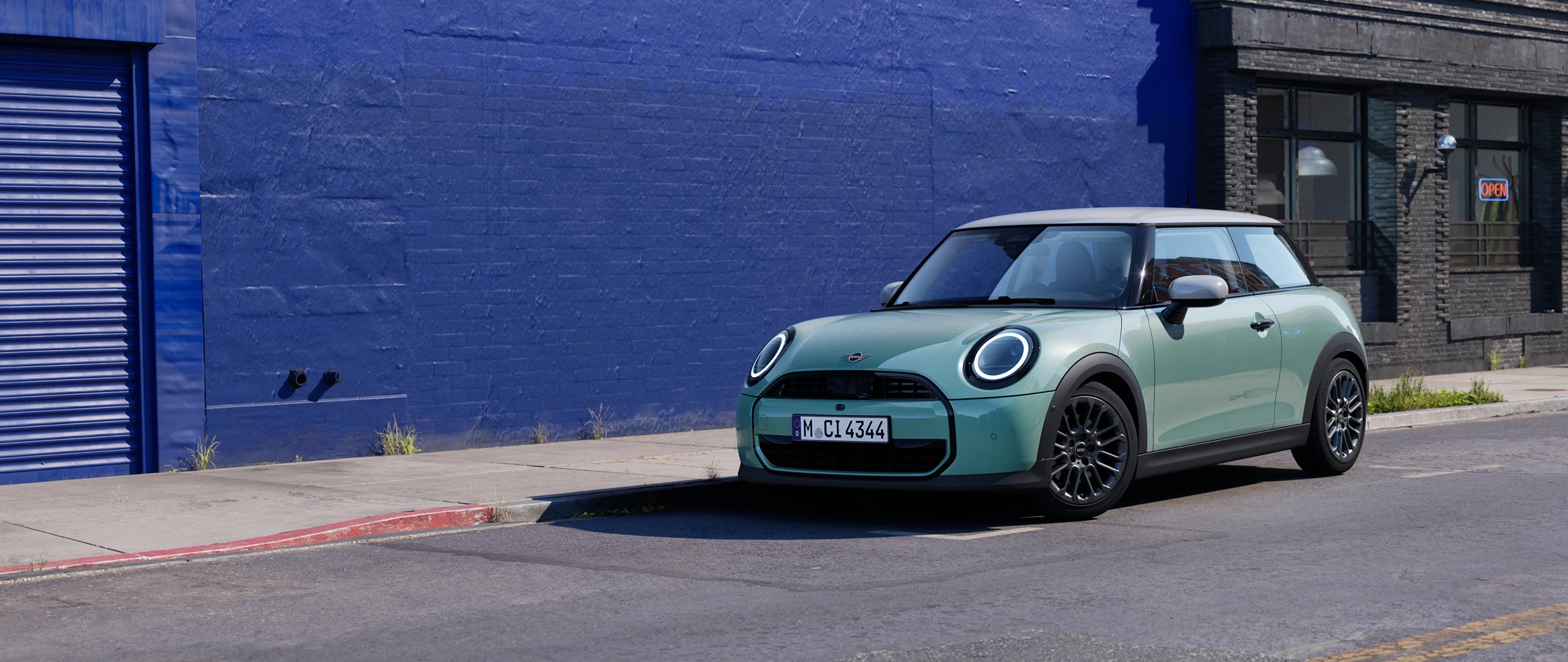 MINI Cooper in Ocean Wave Green parked on an urban street beside a blue wall.