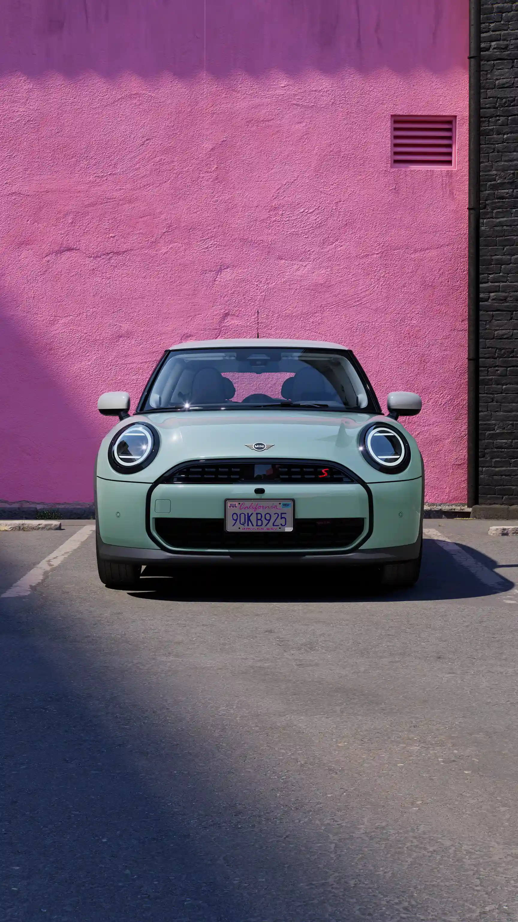 Front view of a MINI Cooper in Ocean Wave Green parked against a bright pink wall.