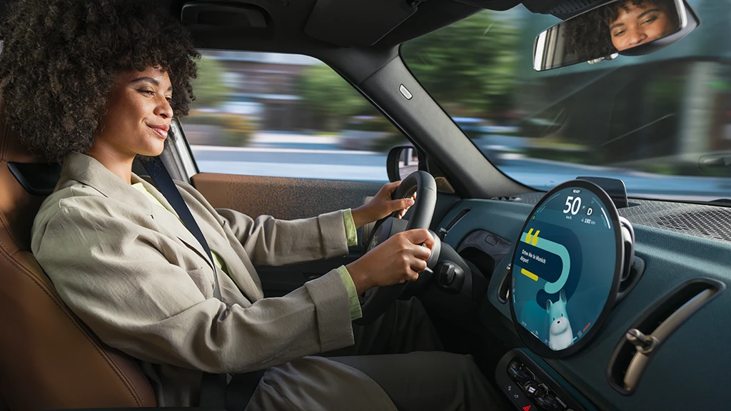Driver holding the steering wheel of a MINI while the round display shows speed and navigation.
