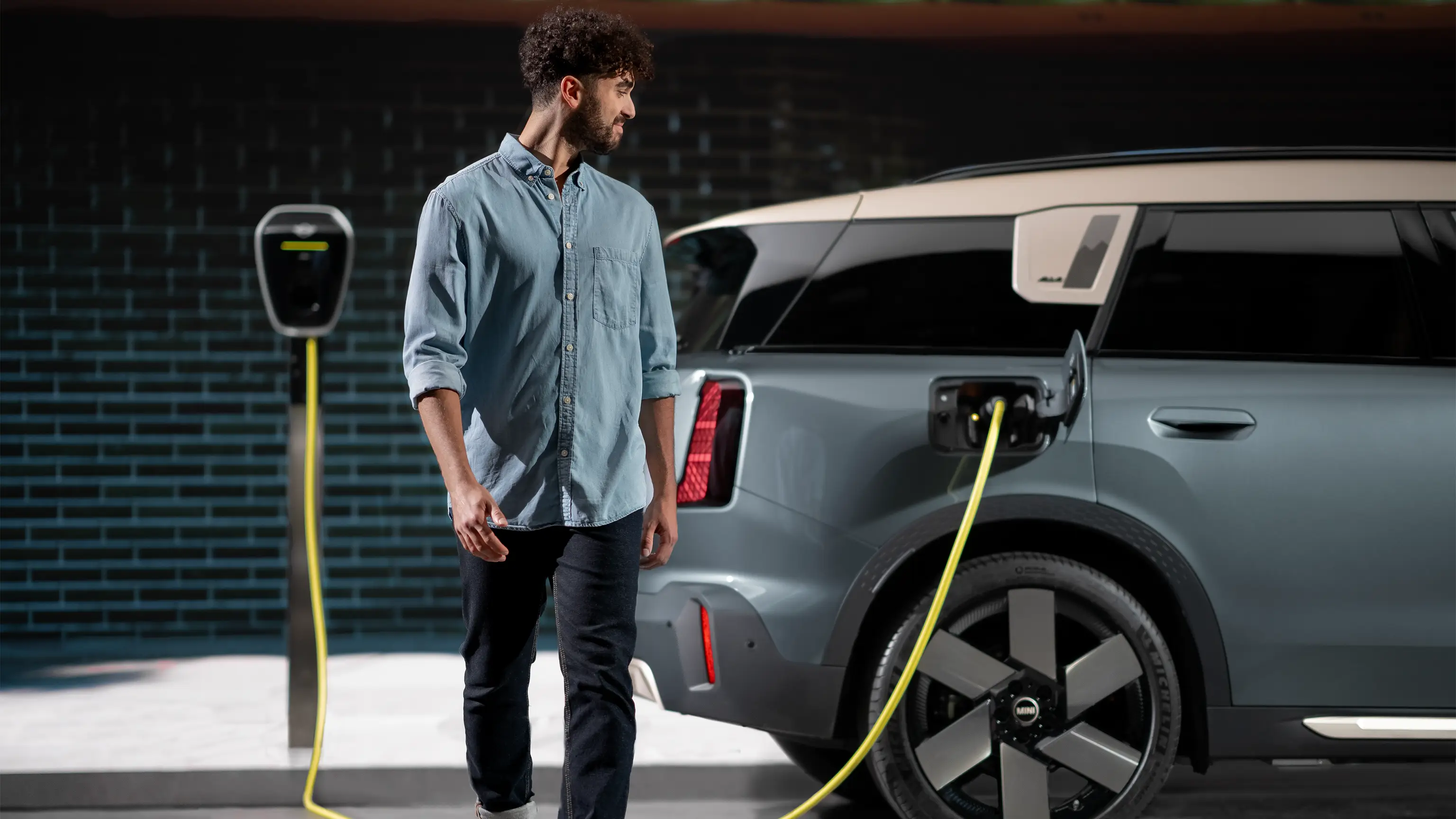 Une personne marchant à côté d’une MINI Countryman en cours de recharge, connectée à une wallbox domestique.