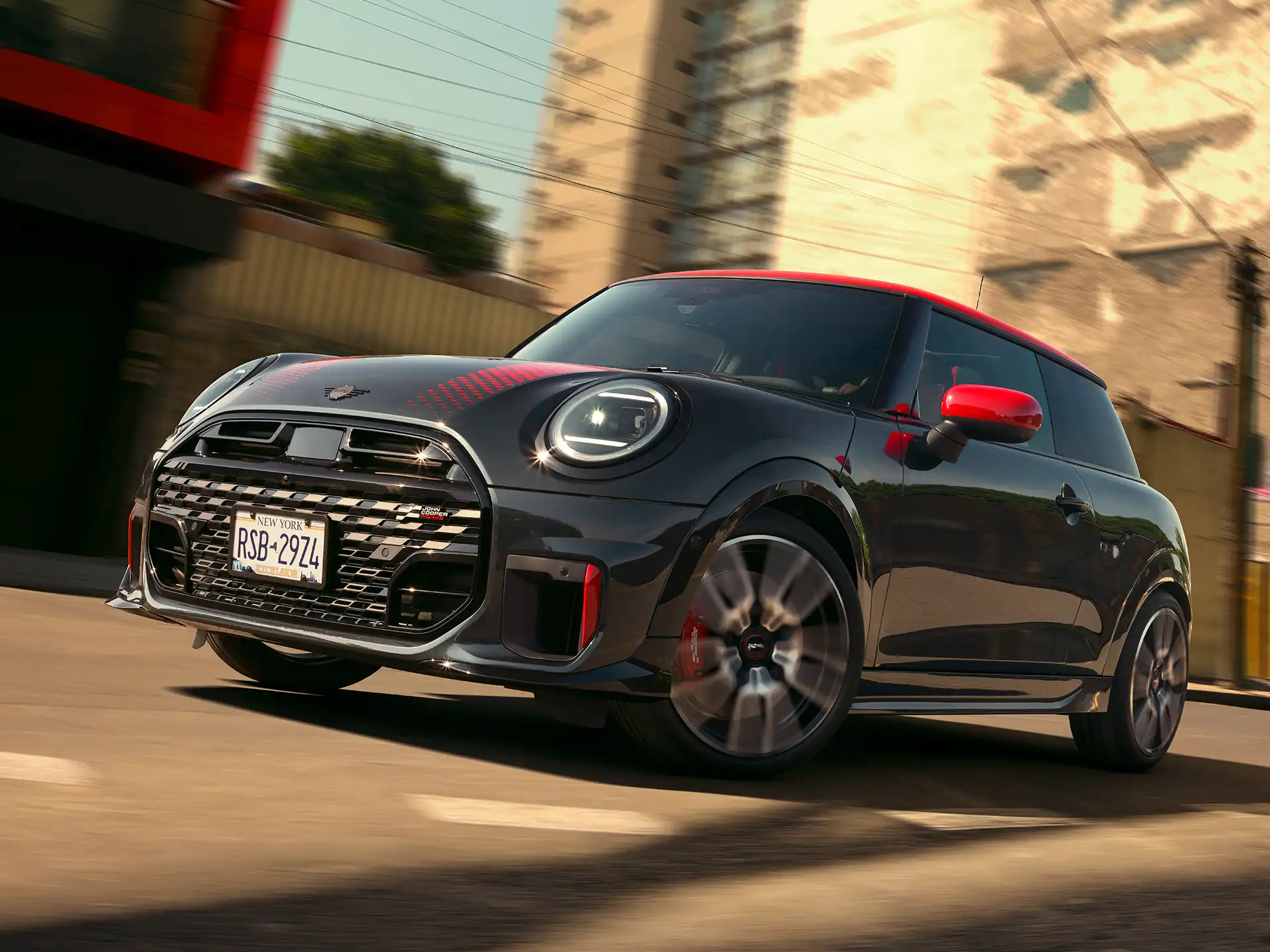 MINI John Cooper Works in Midnight Black II with Chili Red roof driving on an urban road.