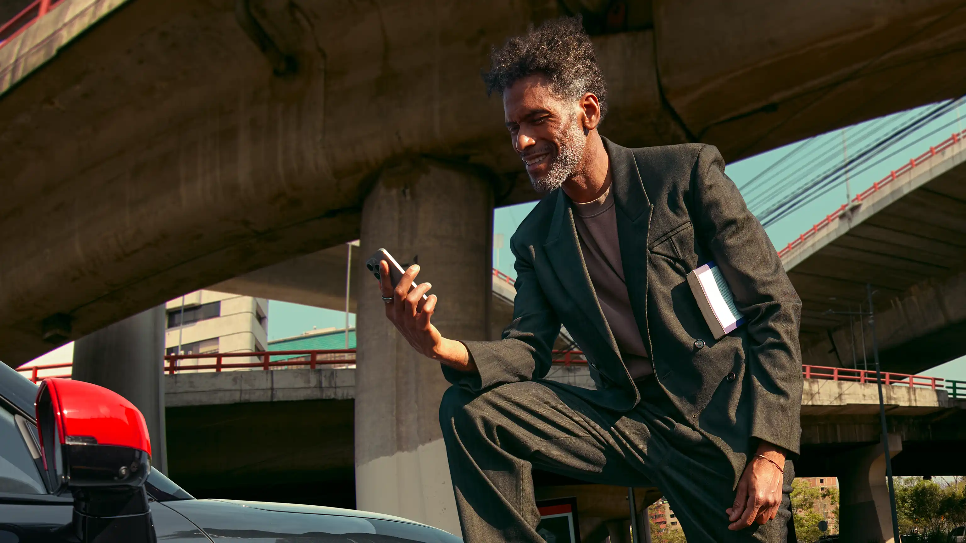Person standing next to a MINI John Cooper Works while looking at a smartphone under an overpass.